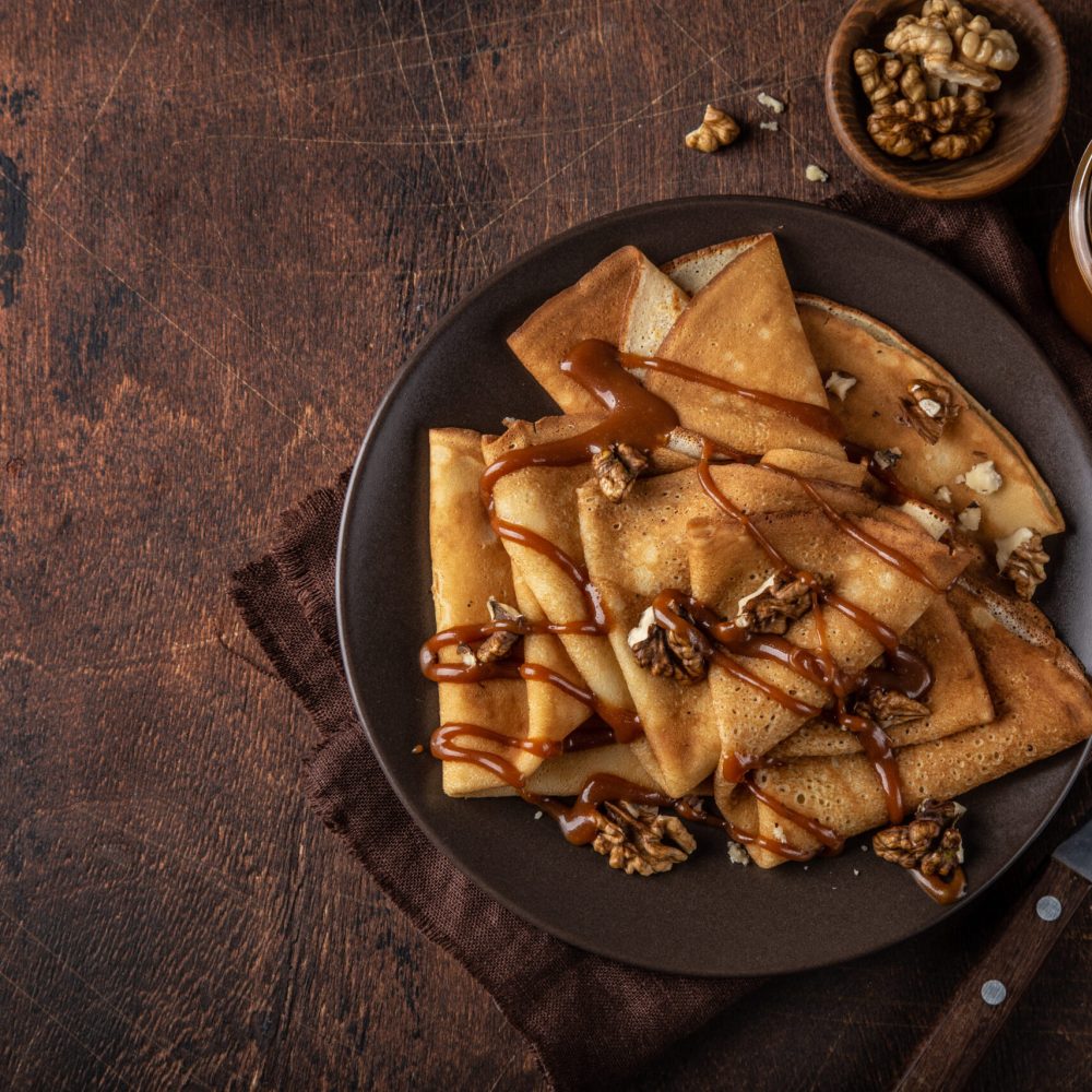 crepes with salted caramel and nuts, top view, wooden background, copy space