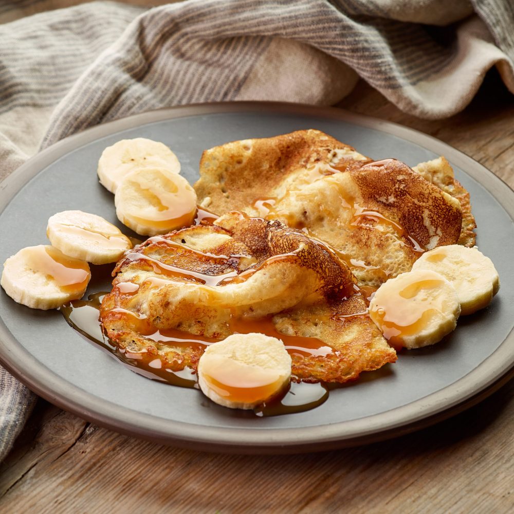 Crepes with banana and caramel sauce on wooden table